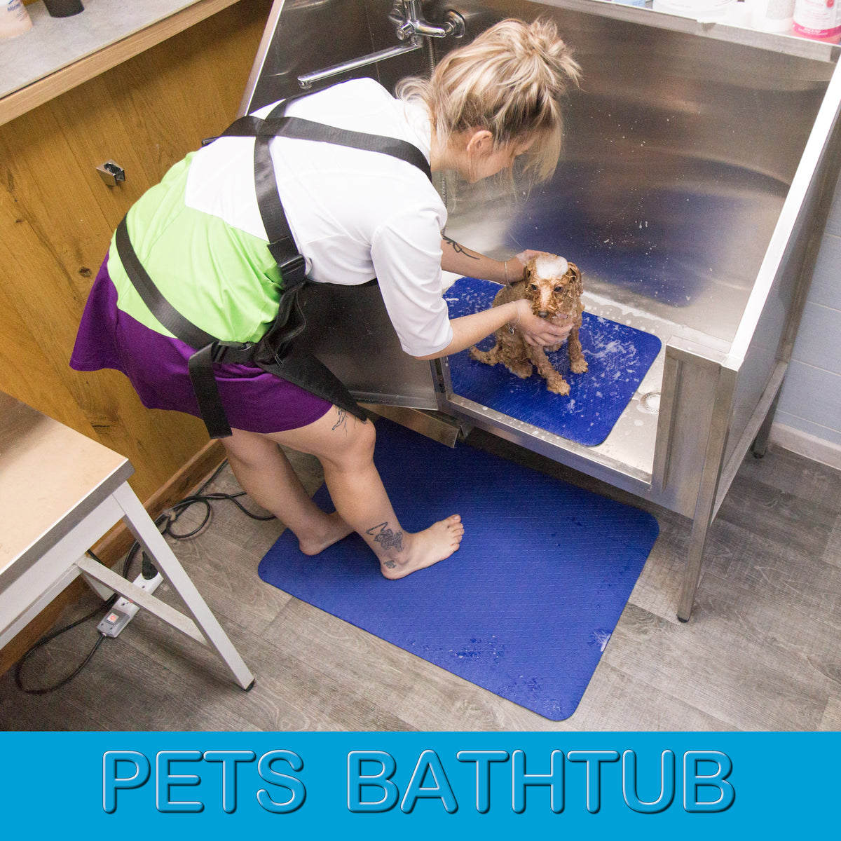 Dark blue non-slip grooming mats used in a pet bathtub and under a groomer’s feet for safer, more comfortable grooming
